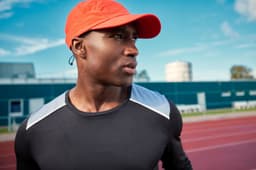 A long-sleeve men's running shirt in black with light grey accents, worn by a man in an orange cap.
