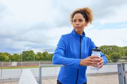 A blue structured fleece jacket is worn by a woman holding a drink bottle, set against an outdoor background.