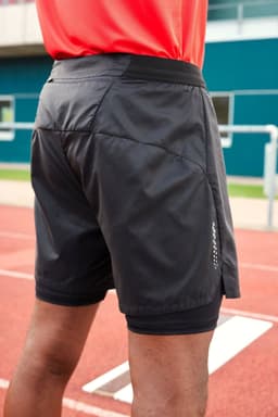 Men's running shorts in black, featuring a logo and a lightweight design, viewed from the back on a track surface.