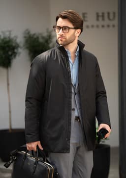 A black men's jacket is worn by a man holding a bag, set in a modern outdoor environment.