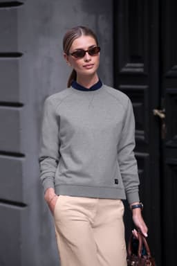 A woman wearing a grey sweatshirt and beige pants, accessorised with sunglasses and carrying a brown bag.