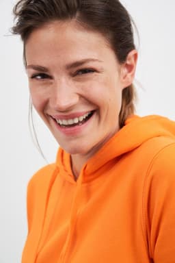 An orange hooded sweatshirt worn by a smiling woman, featuring a hood and a comfortable fit.