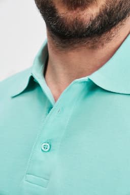 A close-up of a man's neck and collar wearing a mint green polo shirt with a button detail and logo.