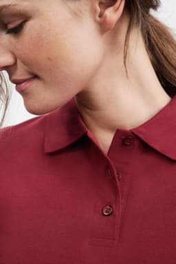 A maroon polo shirt featuring a collared neckline and button details, worn by a model displaying a profile view.