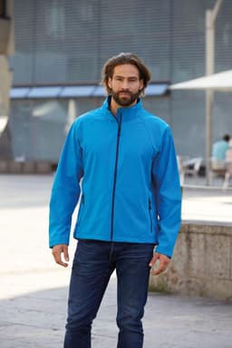 A man in a bright blue softshell jacket standing outdoors, paired with jeans. The jacket features a collar and zip.