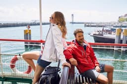 A red and white maritime jacket worn by two people on a boat near the water, with boats and a pier in the background.
