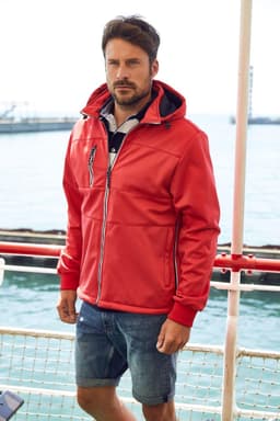 A red men's maritime jacket with a hood, featuring a logo, worn by a man near water.
