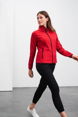 A red ladies softshell jacket with a zip front and two side pockets, paired with black pants.