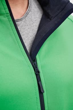 A green softshell jacket featuring a black hood and zipper detailing, with a grey shirt visible underneath.