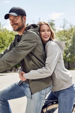 A grey ladies hooded softshell jacket worn by a woman with a man in a green jacket, both smiling outdoors.