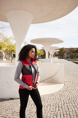 A woman wearing a red and grey fleece vest stands outdoors near modern architectural features.