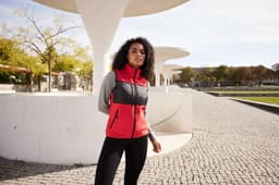 A fleece vest in red and grey, featuring zippered pockets and a logo, worn by a model outdoors.