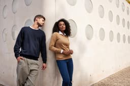 A navy blue and a tan knitted jumper are displayed on models standing against a textured white wall with circular cutouts.
