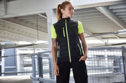 A black vest with neon green accents, featuring a zippered front and pockets. It includes a logo on the fabric.