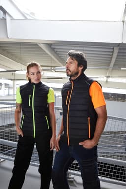 A black vest with neon orange and green accents, worn by two people in a modern indoor setting.