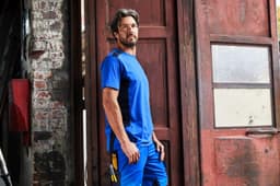 A blue men's workwear T-shirt displayed on a model in an industrial setting, featuring a logo.