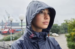 A rain jacket in navy blue worn by a person with a hood, set against a waterfront background.
