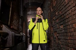 A high-visibility work jacket in yellow and black with a logo, set against a textured brick background.