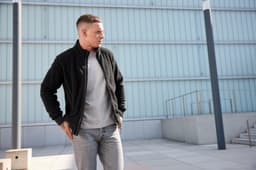 A polar fleece jacket in black, worn by a man, paired with a grey top and light jeans, set against a modern backdrop.