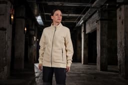 A cream Sherpa jacket with a full zip and side pockets is displayed in an industrial setting.