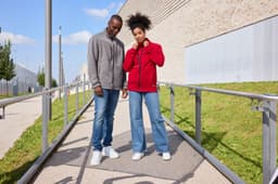 A red fleece jacket and a grey fleece jacket worn by a couple, standing on a pathway with greenery and a building in the background.