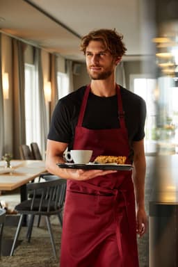 A maroon apron with bib displayed on a model holding a tray with a coffee and food in a restaurant setting.