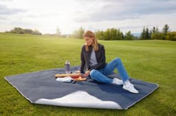 A picnic blanket in navy and white, laid out on grass with a woman sitting, surrounded by snacks and a drink bottle.