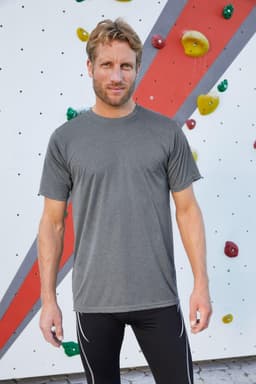 A grey men's active T-shirt displayed on a model in front of a colourful climbing wall. The shirt has a logo.