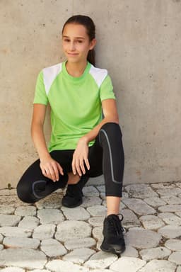 A green T-shirt with white shoulder panels, paired with black leggings and sneakers, displayed on a model.