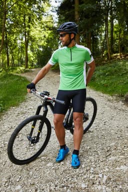 A man stands beside a mountain bike, wearing a green and white half zip cycling shirt and black shorts.