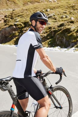 A man wearing a black and white cycling shirt with a helmet, riding a bicycle on a scenic mountain road.