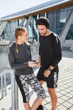 A pair of models wearing a grey long-sleeved ladies sports shirt and matching activewear. The shirt features colour detailing.