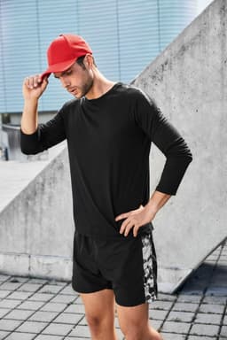 A man wearing a black long-sleeve sports shirt and shorts, complemented by a red cap, poses outdoors.