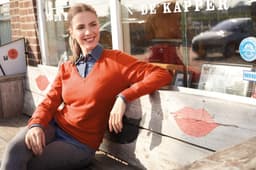 A woman wearing an orange ladies V-neck pullover sits on a wooden bench outside a café.