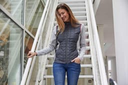 A grey and black ladies' knitted hybrid jacket, featuring a zip front and pockets, displayed outdoors on a staircase.