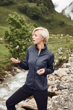 A navy ladies knitted fleece jacket is worn by a woman outdoors, with a scenic backdrop of greenery and a stream.