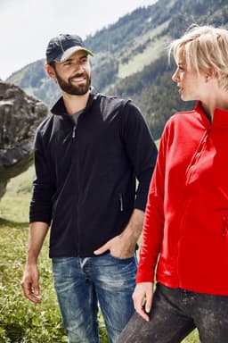 A couple stands outdoors wearing jackets; one in black and the other in red, with a logo on the jackets.