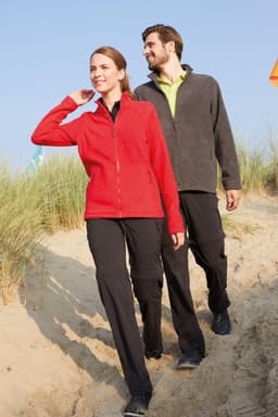 A red fleece jacket worn by a woman, accompanied by a man in a grey fleece jacket, walking on sandy terrain.