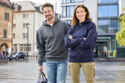 A grey half zip hoodie on a man and a navy hoodie on a woman, both in an urban setting.