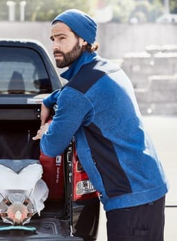 A blue knitted fleece jacket paired with a navy beanie, worn by a man leaning against a truck.