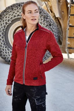 A red polar fleece jacket with a front zip and contrasting details, worn by a model in a work setting.