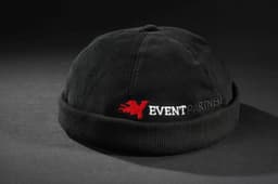 A black 6 panel chef cap with a folded brim and a logo featuring red text on the front.
