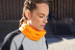 A headband in bright orange, worn as a neck gaiter by a woman in a grey athletic top. Features a logo.