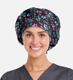 A bouffant cap featuring a black background with colourful floral and paw print patterns. The model is smiling.