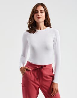 A long-sleeve white baselayer top displayed on a model, paired with pink trousers. The image features a logo.