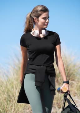 A black women's t-shirt worn by a woman with headphones, paired with green leggings and a casual bag.