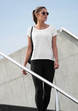 A white women's t-shirt is paired with black leggings, worn by a model walking down a staircase.