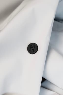 A close-up of a white jacket fabric featuring a black circular button with the letter "N" embossed on it.