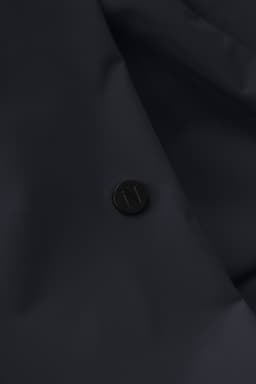 A close-up of a dark navy jacket featuring a round black logo button.