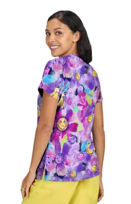 A colourful purple top featuring a playful floral and smiley face pattern, with a woman smiling while wearing it.
